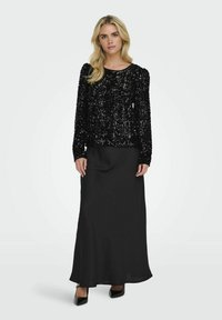 Haut à manches longues noir pailleté associé à une jupe maxi en satin noir fluide, dotée d'un col rond et d'une texture douce. Des talons noirs complètent le look.