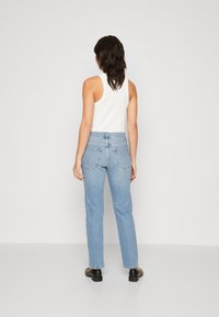 Ljusblå raka jeans med hög midja, bakfickor och en vit ärmlös ribbad topp. Svarta skor avslutar outfiten.