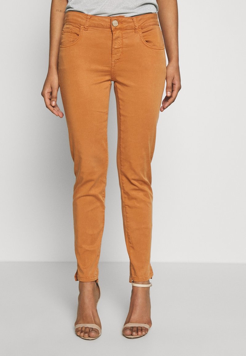 Pantalon ajusté orange avec une fermeture boutonnée à l'avant, quatre poches et une texture lisse. L'ourlet présente un léger détail retourné.