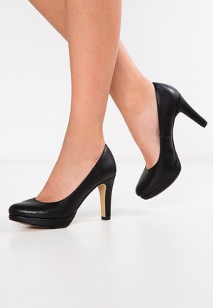 Zwarte leren hoge hakken met een ronde neus en een hak van 10 cm, voorzien van een contrasterende beige accent aan de basis van de hak. Glad textuur.