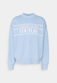 Ljusblå sweatshirt i bomull, med ribbad mudd och nacke. Broderad text "VERSACE JEANS COUTURE" i vitt och rosa.