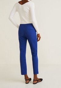 Haut blanc à manches longues côtelé assorti d'un pantalon bleu ajusté avec une poche arrière, porté avec des sandales plates noires. Design simple et épuré.