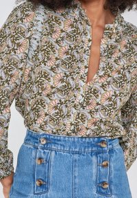 Blus med blommönster i ljusblått, med rosa och gröna mönster, knappslå och rynkad halsringning. Körd ihop med en högmidjad jeanskjol.