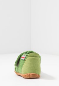 Zieloney klapek wykonany z miękkiego, teksturowanego materiału z rzepem, gumową podeszwą i wyściełanym tyłem dla komfortu. Dołączona czerwona metka marki.