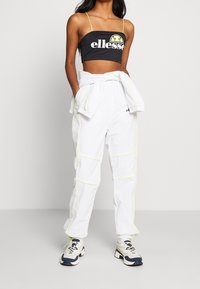 Haut court noir avec logo, pantalon cargo blanc avec piping jaune néon, et baskets multicolores. Allie un design sportif et décontracté.