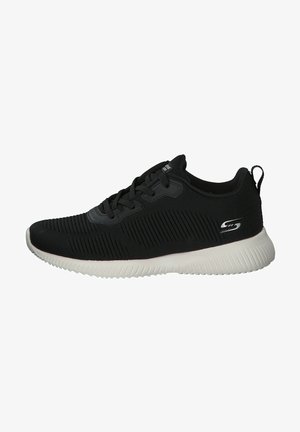 Zapatilla deportiva negra con parte superior texturizada, que presenta detalles acanalados, diseño de cordones y una suela de goma blanca y flexible. Acabado en plata del logo en el lateral.