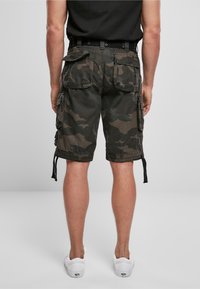 Pantalones cortos cargo de camuflaje en verde oscuro y negro. Cuenta con múltiples bolsillos grandes y cordones en el dobladillo. La tela es duradera y texturizada.