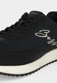 Baskets noires avec lacets noirs, semelle blanche et logo brodé blanc "Boss" sur le côté et la languette.