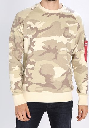 Tarnmuster-Sweatshirt in Beige und Hellbraun, aus weichem Stoff, mit Rippbündchen und Saum, sowie einem Patch auf der Brust.