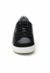 Black sneaker with perforated leather upper, padded tongue, and contrasting white rubber sole. Standard lace-up closure. Flat design.
