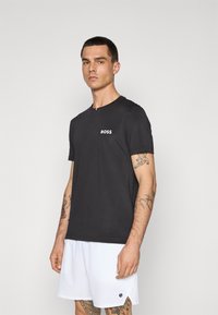 Svart t-skjorte med korte ermer og rund hals, med hvit "BOSS"-logo på brystet, sammen med hvite shorts med et rundt logo.
