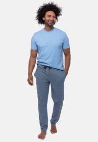 T-shirt en coton bleu clair associé à un pantalon de pyjama bleu à motifs avec taille à cordon ; le modèle est pieds nus et souriant.