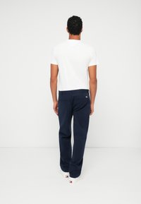 Ναυτικά μπλε βαμβακερό παντελόνι με ίσια γραμμή, τέσσερις τσέπες και μια μικρή ετικέτα με το λογότυπο. Συνδυάζεται με λευκό μπλουζάκι με στρογγυλή λαιμόκοψη.