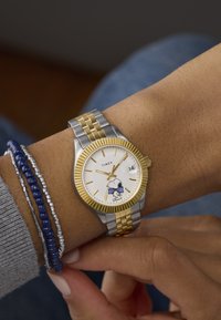 Timex wristwatch with a silver and gold metal band. White dial features Snoopy illustration and gold hour markers. Date display at 3 o'clock.