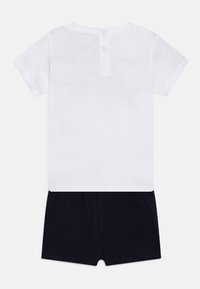 White cotton short-sleeve top with two button closure at the back, paired with navy blue shorts made of soft fabric, featuring an elastic waistband.