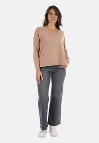Maglione beige a scollo a v con maniche lunghe e una vestibilità ampia, abbinato a jeans svasati blu scuro e sneakers bianche. Design semplice e minimalista.