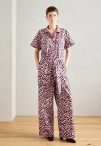 Rózsaszín leopárd mintás overál r�övid ujjakkal, gombos elejével, derékmegkötővel és széles szárakkal. Az anyag könnyűnek és simának tűnik. Fekete részletek az egész ruhán.