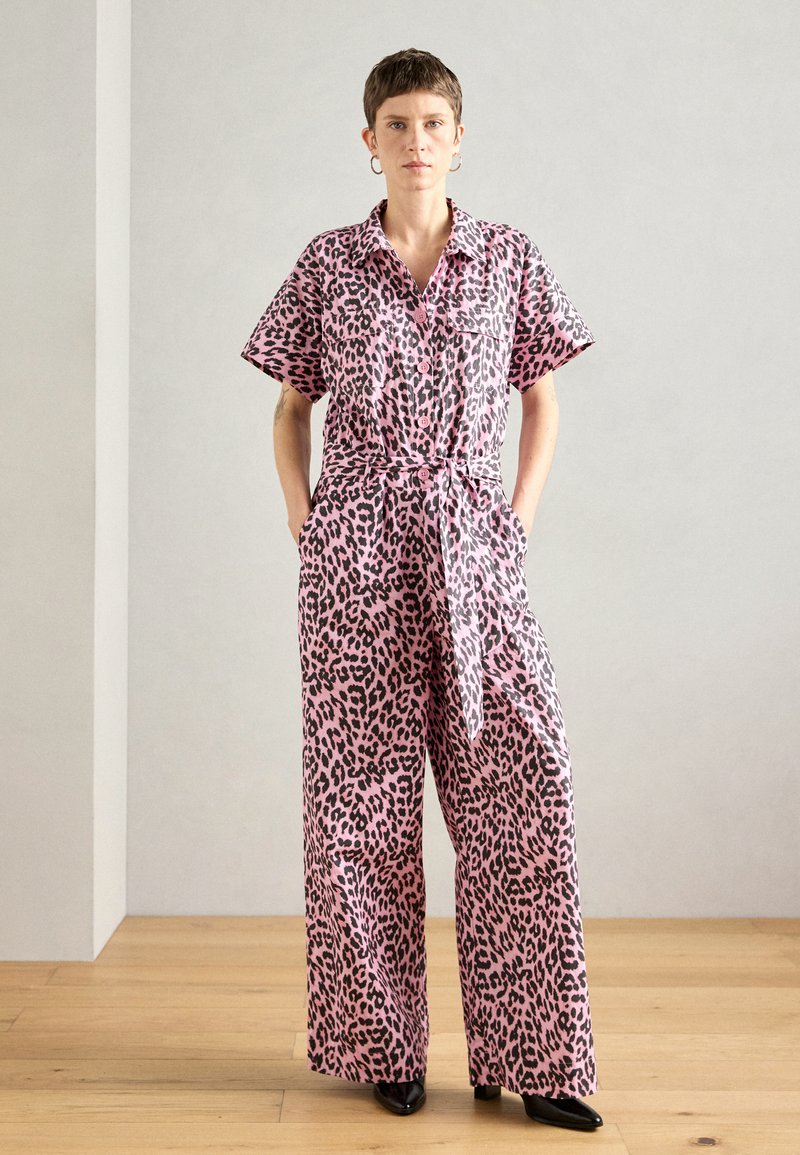 Rózsaszín leopárd mintás overál rövid ujjakkal, gombos elejével, derékmegkötővel és széles szárakkal. Az anyag könnyűnek és simának tűnik. Fekete részletek az egész ruhán.