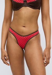 Κόκκινο κάτω μέρος μπικίνι με μικρό άσπρο ανθικό μοτίβο, αντίθετη καφέ λεπτομέρεια και ψηλό κόψιμο που αναδεικνύει τη μέση και τα πόδια.