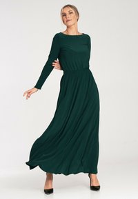 Zielona długa sukienka maxi z długim rękawem, dopasowaną talią i zwiewnym dołem, wykonana z miękkiego materiału, z dekoltem typu łódka i gładką strukturą.