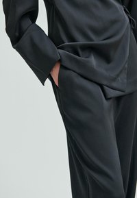 Czarny zestaw satynowy składający się z bluzki z długim rękawem o luźnym kroju oraz spodni z bocznymi kieszeniami. Gładka tekstura z miękkim układem.