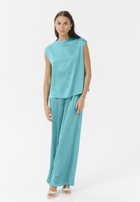 Ensemble deux pièces turquoise comprenant un haut sans manches ample et un pantalon à jambes larges, fabriqué en matériau léger avec une texture douce.