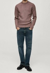 Gestrickter hellrosa Pullover mit Rundhalsausschnitt, kombiniert mit dunkelblauen Jeans mit geradem Bein und schwarzen Schuhen. Strukturierter Stoff mit gerippten Bündchen.