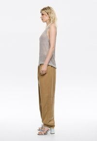 Top senza maniche argento, pantaloni beige a gamba larga e sandali con tacco alto argento. Il top presenta un tessuto lucido e testurizzato.