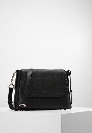 Czarna, teksturowana torebka na ramię DKNY ze skóry, z klapką zamykającą, regulowanym paskiem i srebrnym łańcuszkiem, na białej powierzchni.