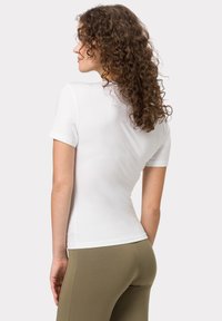 Weißes, tailliertes T-Shirt mit kurzen Ärmeln, glatter Textur, rundem Halsausschnitt und einem Rückennahtdetail, kombiniert mit olivgrünen Leggings.