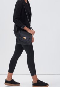 Czarna skórzana torba noszona na krzyż z zaokrąglonym klapkiem i złotymi detalami. Strukturalny czarny sweter o dopasowanym kroju oraz czarne skinny jeans.