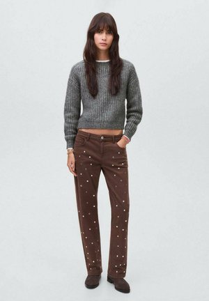 Grau gerippter Pullover, braune Hose mit metallischen Punktverzierungen, gerade geschnitten, Stoffstruktur sichtbar, kombiniert mit dunklen Schuhen.