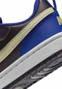 Czarny i niebieski sneaker o teksturowanej powierzchni, z beżowym paskiem i białą podeszwą środkową. Charakterystyczne detale to niebieskie sznurówki oraz wzorzysta podeszwa zewnętrzna.