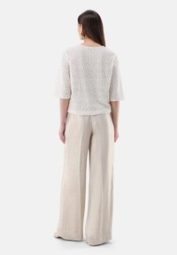 Weißes, strukturiertes Oberteil mit kurzen Ärmeln, kombiniert mit hellbeigen, weiten Hosen mit einem dezenten Glanz und einem weichen, fließenden Stoff.