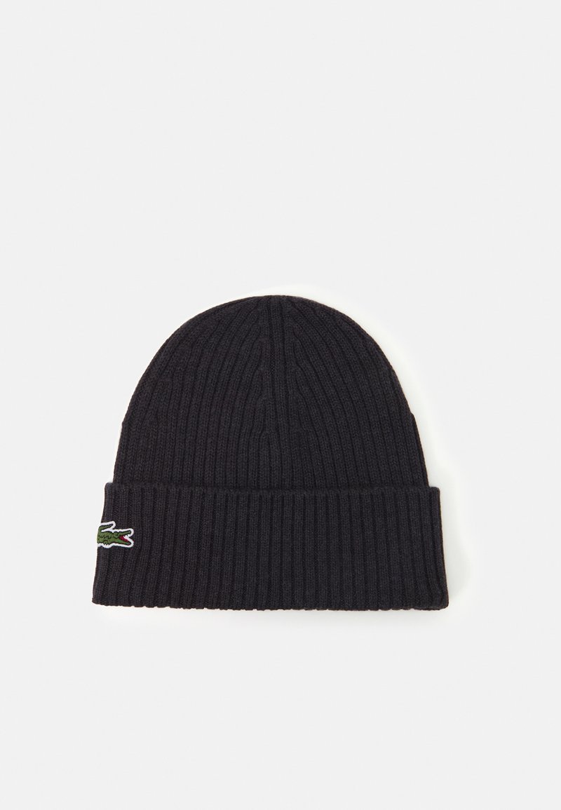 Svart ribbestrikket lue med oppbrettkant, med en liten grønn krokodille-logo på siden. Myk tekstur, uformelt design.