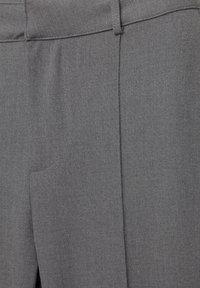 Pantalon gris sur mesure avec une texture lisse, coupe droite, poche avant et un pli discret courant le long de chaque jambe.