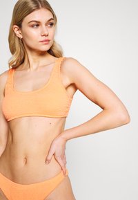Oransje cropped bikini topp med teksturert stoff og brede skulderstropper, paret med matchende lavtsittende truser. Glatt, sømløs design.
