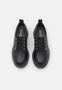 Chaussures noires en cuir vegan avec un bout rond, six œillets en métal, semelle en caoutchouc texturé et une languette à l'arrière pour un enfilage facile.