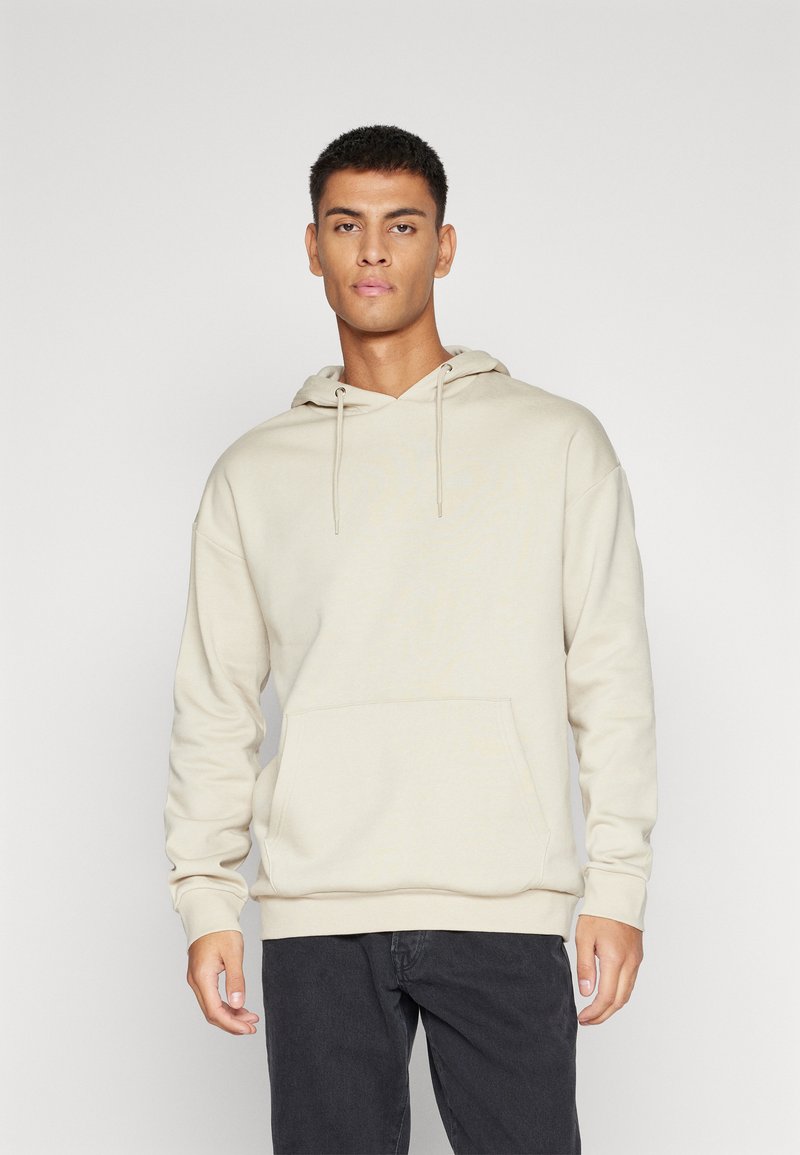 Beige hættetrøje med en frontlomme, snoretræk og ribbede manchetter. Stoffet virker glat med en afslappet pasform.