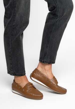 Braune Leder-Fahrschuhe, getragen mit gekürzten schwarzen Jeans, die die strukturierten Sohlen und die Schnürdetails der Schuhe zeigen.