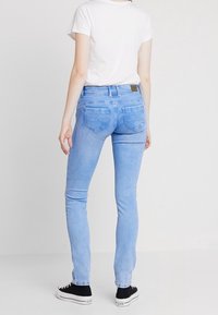 Světle modré úzké džíny s klasickým designem pěti kapes, vysokým pasem, mírným vyblednutím a hnědou koženou nášivkou na zadním pásu.