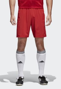 Rote Sportshorts mit elastischem Bund, kombiniert mit weißen Kniestrümpfen mit drei schwarzen Streifen und schwarzen Fußballschuhen.