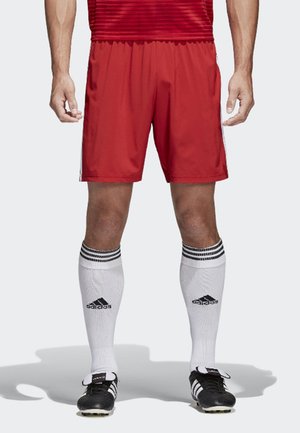 Pantaloncini sportivi rossi con elastico in vita, abbinati a calze bianche fino al ginocchio con tre strisce nere e scarpe da calcio nere.