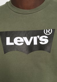 T-shirt en coton vert olive présentant un grand logo Levi's noir sur le devant, avec une police blanche et un accent de marque dans le design.