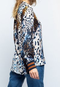 Blusa de manga larga en una tela sedosa, con un estampado animal multicolor que presenta patrones en azul, negro y marrón, y puños a rayas.
