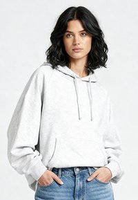 Lichtgrijze hoodie van zachte stof met een voorvak, verstelbare trekkoordkap en een ontspannen pasvorm. Gecombineerd met lichtblauwe spijkerbroek.