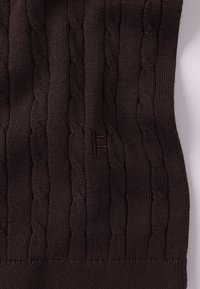 Καφέ πλεκτό κασκόλ με σχέδιο καλώδιο, υφή με ριμπ και μικρή ετικέτα λογότυπου διακριτικά ενσωματωμένη στο ύφασμα.