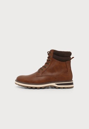 Bottine en cuir marron à lacets avec col rembourré marron foncé et semelle beige robuste sur un fond uni.