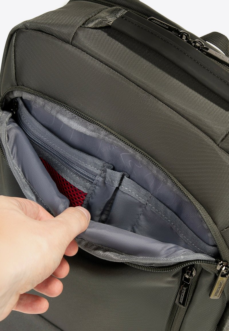 Grijze stoffen rugzak met een open ritstas, die een gaascompartiment en organisatienummers in een lichter grijs interieur onthult.