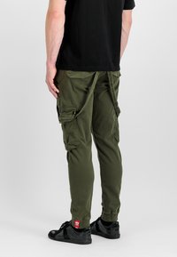 Cargo byxor i olivgrön, med flera fickor, en tapered design och justerbara vristhällor. Matchas med svarta sneakers.